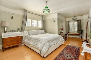 A bedroom with a bed, dresser, bedside table, lamp, curtains, and a hanging light fixture.