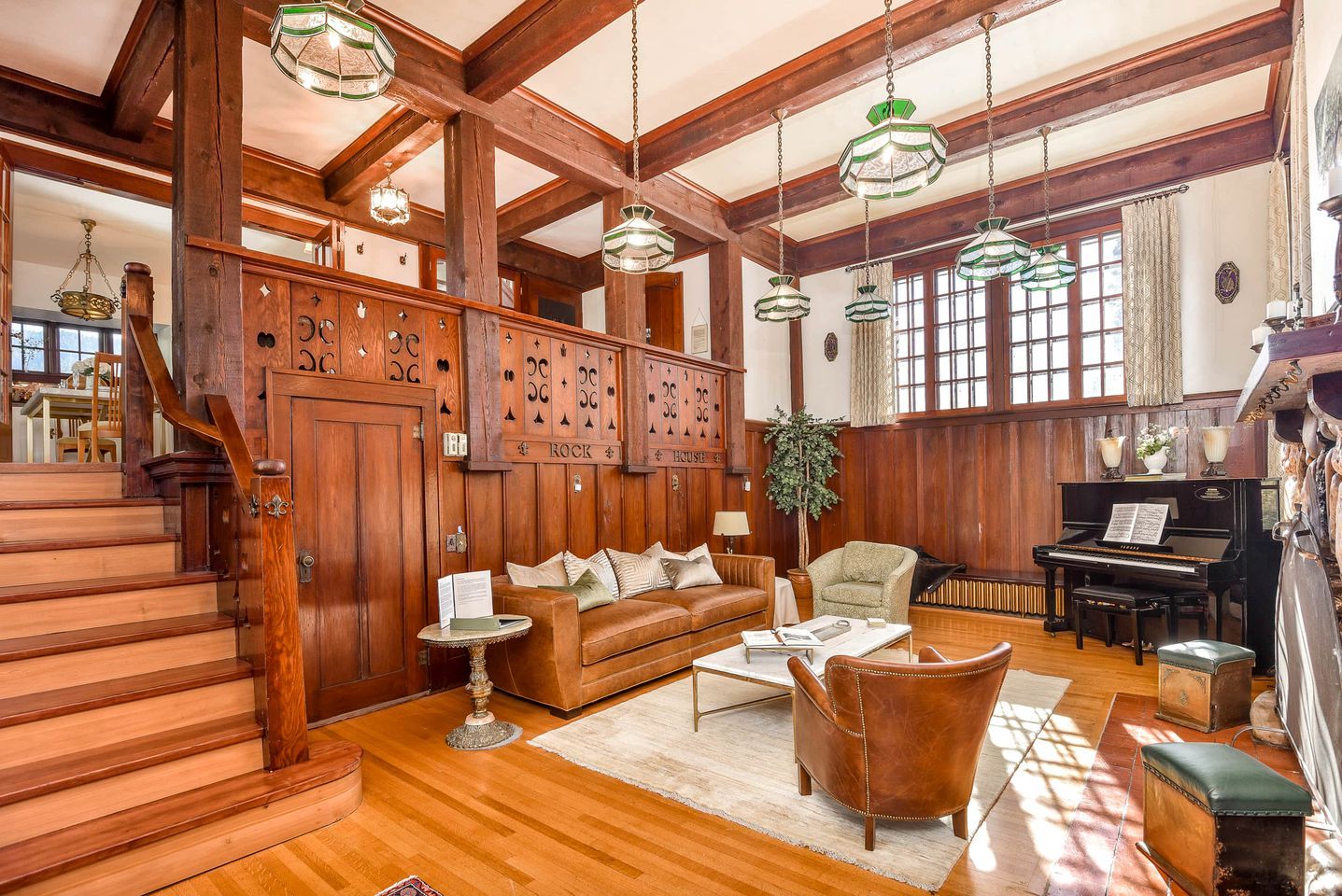 A spacious living room with a grand staircase, wooden paneling, a piano, and a cozy seating area.