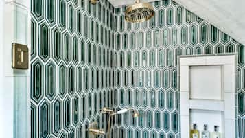 Un baño con pared de diseño geométrico, ducha con detalles dorados y puerta blanca con artículos de aseo.