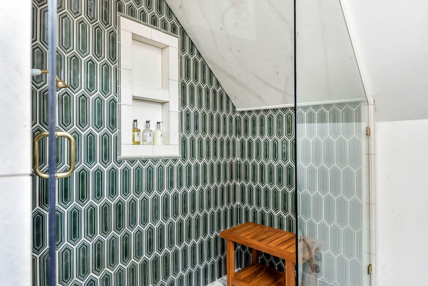 Een badkamer met een wand betegeld met een geometrisch patroon, een klein houten plankje en een raam met toiletartikelen.