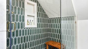 Een badkamer met een wand betegeld met een geometrisch patroon, een klein houten plankje en een raam met toiletartikelen.