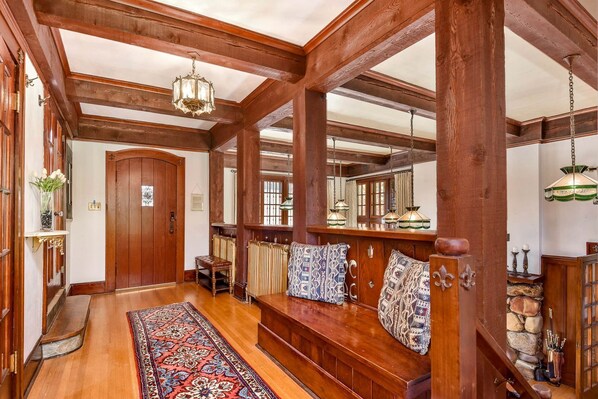 A wooden hallway with a bench, patterned rug, and hanging lamps.