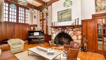 Un salón amplio con chimenea de piedra, vigas de madera, un piano y sillones de cuero.