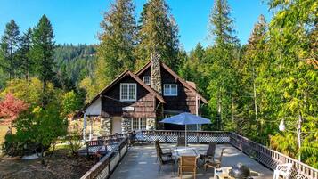 A cabin with a stone chimney, wooden exterior, and a patio with outdoor furniture.