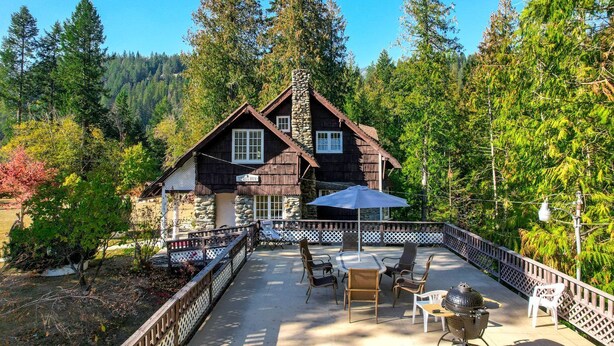 Une cabane dotée d’une cheminée en pierre, d’un revêtement extérieur en bois et d’une terrasse aménagée avec du mobilier d’extérieur.