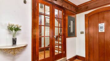Una puerta de madera con paneles de vidrio, una pared blanca y un estante con un jarrón de flores.