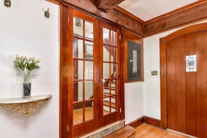 A wooden door with glass panels, a white wall, and a small shelf with a vase of flowers.