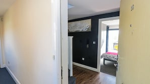 A hotel room with a wooden floor, a bed with a patterned bedspread, a black wall, and a door with a number. - Rickman Apartment (Birmingham)