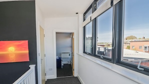 A hallway with a view of a bedroom, a radiator, and a window with a view of buildings. - Rickman Apartment (Birmingham)
