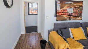 A living room with a grey sofa, a yellow throw blanket, a clock, and a framed picture of a bridge. - Rickman Apartment (Birmingham)