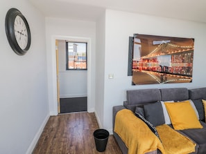 A living room with a grey sofa, a yellow throw blanket, a black clock, and a framed picture of a bridge. - Rickman Apartment (Birmingham)