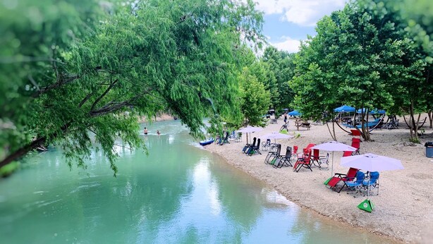 A riverside setting with a sandy beach, trees, and outdoor seating. - Incredible Safari Tent with Barbecue in Staples, Texas (Staples)