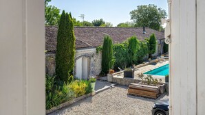 A courtyard with a swimming pool, a stone wall, and a variety of greenery. - Bed and Breakfast 'Chambre Orée Du Jour' with Shared Terrace, Shared Garden and Wi-Fi (Saint-Porchaire)