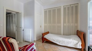 A small room with a single bed, a radiator, a wardrobe with louvered doors, and a striped chair. - Bed and Breakfast 'Chambre Orée Du Jour' with Shared Terrace, Shared Garden and Wi-Fi (Saint-Porchaire)