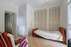 Una stanza piccola con un letto singolo, un termosifone, un armadio con ante a persiana e una sedia a righe.
