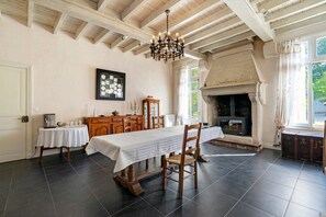 A dining room with a long table, chairs, a chandelier, a fireplace, and a view of the outdoors. - Bed and Breakfast 'Chambre Plein Sud' with Shared Terrace, Shared Garden and Wi-Fi (Saint-Porchaire)