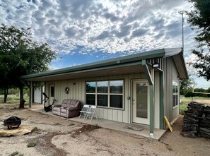 A single-story building with a covered porch, a sliding glass door, a brown leather couch, and a small table.