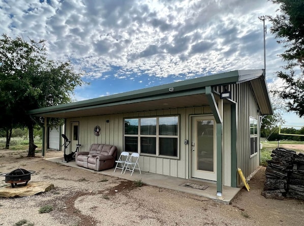 A single-story building with a covered porch, a sliding glass door, a brown leather couch, and a small table.
