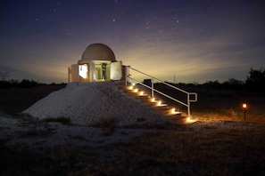 A dome-shaped observatory with a staircase leading up to it, surrounded by a gravel area.