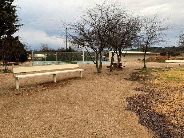 A park with a bench, trees, and a basketball court.