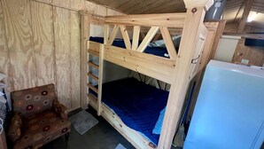 Ein Holzbett mit zwei Himmelsbetten, eine blaue Matratze, ein kleiner Holzstuhl und ein weißer Kühlschrank in einem Raum mit Holzwänden und einer schrägen Decke.