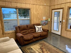 A room with a brown leather sofa, a beige armchair, and a rug with a dinosaur design.