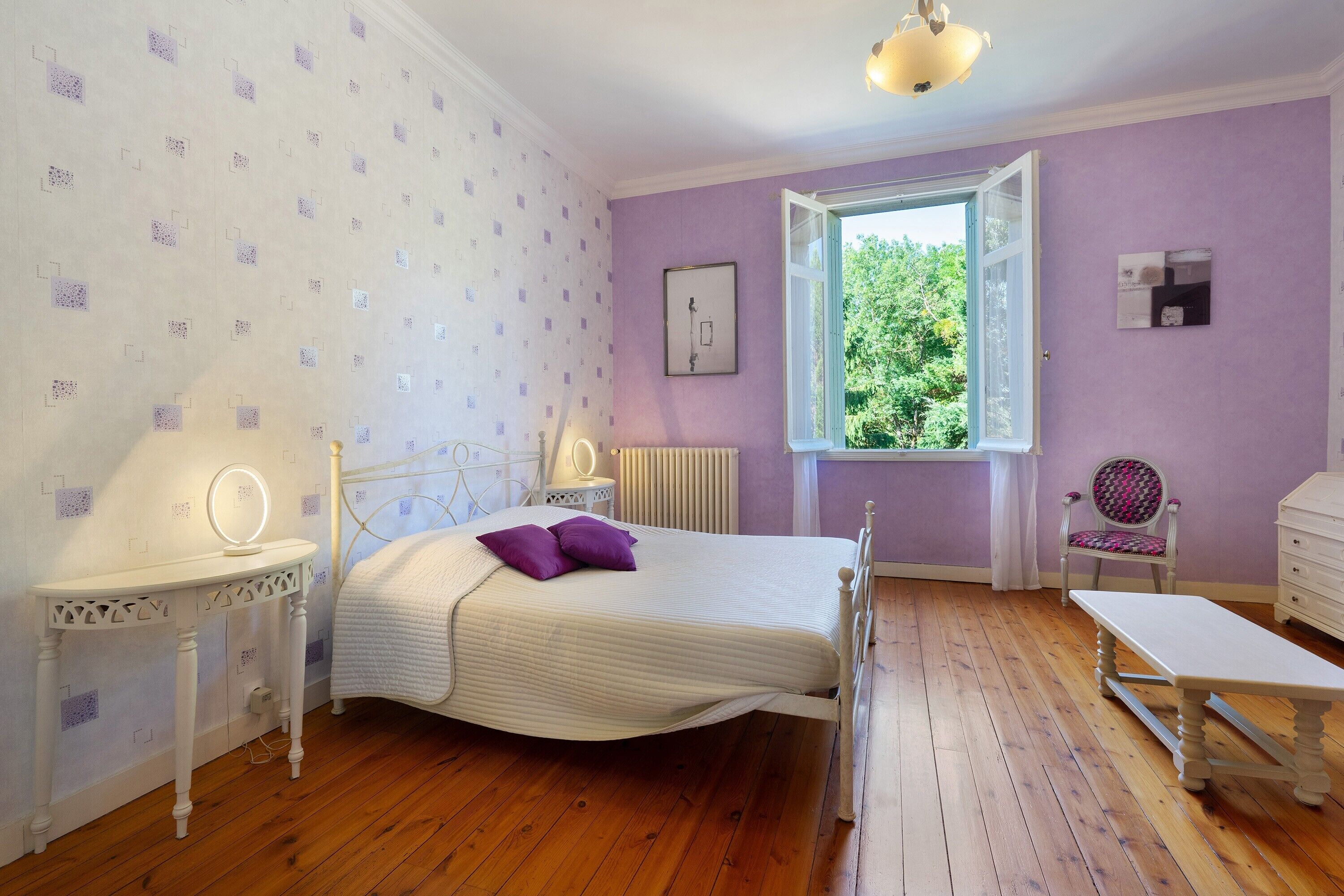 Une chambre à coucher comprenant un lit, une table de chevet avec un miroir, une chaise et une fenêtre donnant sur un paysage verdoyant.
