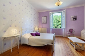 Une chambre à coucher comprenant un lit, une table de chevet avec un miroir, une chaise et une fenêtre donnant sur un paysage verdoyant.