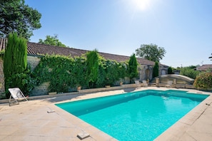 Une piscine dotée d’une terrasse carrelée, entourée de verdure et bordée d’un mur en pierre.