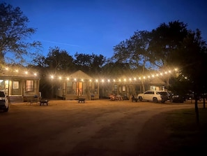 A row of cabins with string lights, outdoor seating, and a dirt ground. - Exciting Glamping Getaway: Comfortable Tented Cabin on the Geronimo Creek in Seguin, Texas (Seguin)