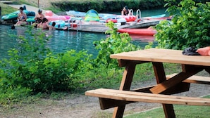 A wooden picnic table by a calm water body with boats and inflatable rings.