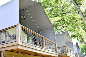 A multi-level building with a balcony, a hanging light fixture, and a tree in the background.