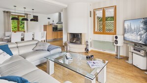 A modern living room with a glass coffee table, a fireplace, a TV, and a kitchen in the background. - House for 8 with bbq, big garden and terrace (Fouesnant)