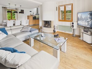 A modern living room with a glass coffee table, a fireplace, a TV, and a kitchen in the background. - House for 8 with bbq, big garden and terrace (Fouesnant)