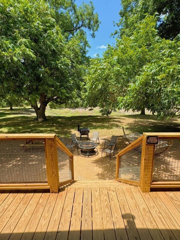 A wooden deck with a fire pit and chairs, surrounded by trees. - Luxury Safari Tent in Texas, Perfect for Glamping in Cibolo (Cibolo)
