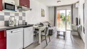 Eine kompakte Küche mit Mikrowelle, Kaffeemaschine und Geschirrspüler. Ein Essbereich mit Tisch und Stühlen sowie ein Balkon mit Fernseher vorhanden.