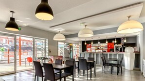 Ein modernes Restaurant mit Barbereich, großen Fenstern und Blick auf umliegende Gebäude.