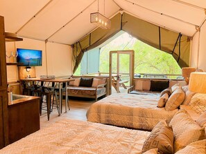 Een tentverblijf met een eethoek, een bed met behang en een televisie.