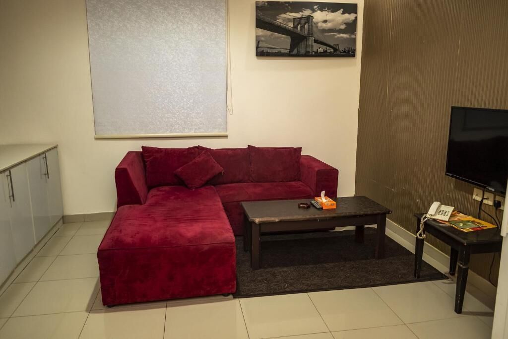 Ein Wohnzimmer mit einem roten Sofa, einem Couchtisch, einem Fernseher und einem gerahmten Bild an der Wand.