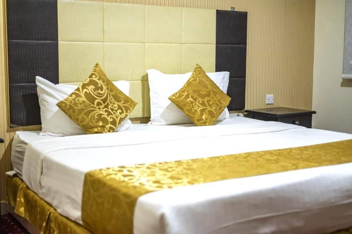 A hotel room with a bed, a nightstand, and a wall-mounted outlet.