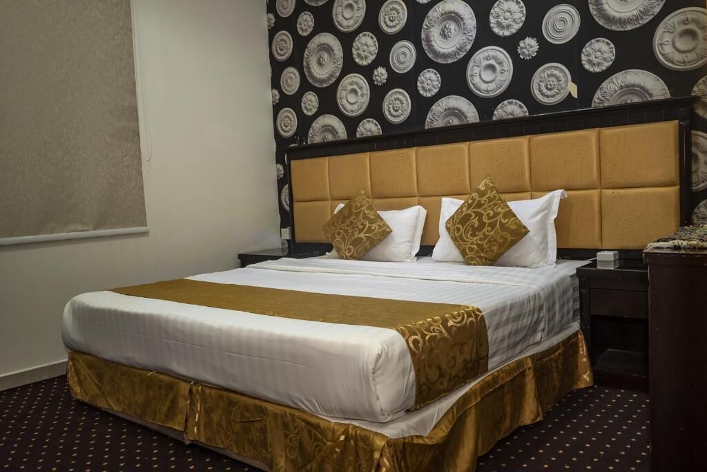A hotel room with a large bed, a headboard, a nightstand, and a patterned wallpaper.