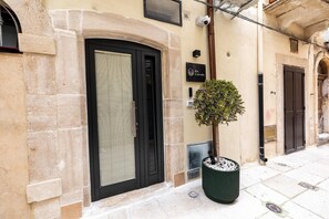 Un bâtiment avec une porte noire, un petit arbre dans un pot et une enseigne avec un logo.