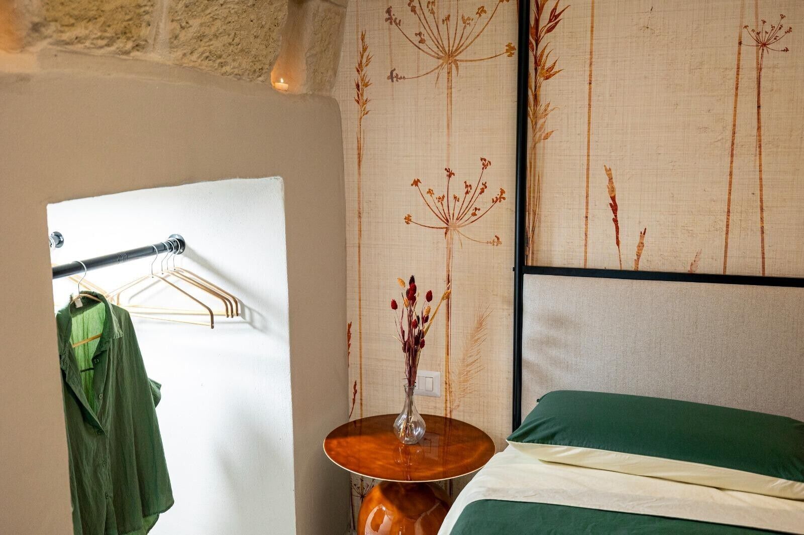 A room with a bed, a wall-mounted shelf with a vase, and a clothing rack.