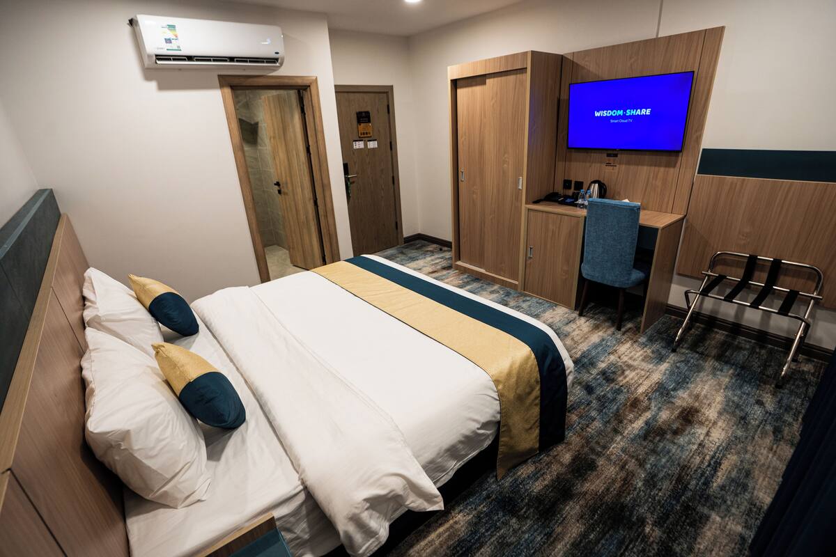 A hotel room with a bed, a desk, a chair, a television, and an air conditioning unit.