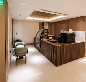 Una zona de recepción moderna con un mostrador de madera, una mampara de cristal y un área de espera con sillas.