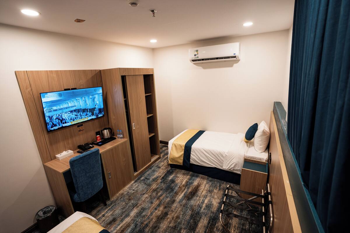 A hotel room with a bed, a desk, a television, a wardrobe, and an air conditioning unit.
