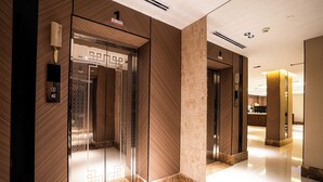 A modern elevator with a glass door, a wall-mounted phone, and a digital display. - Alhijrah View 2 Hotel (Makkah)