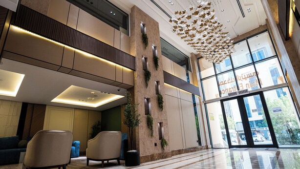 A modern lobby with a high ceiling, a reception desk, seating area, and large windows. - Alhijrah View 2 Hotel (Makkah)