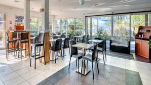A spacious indoor dining area with multiple tables and chairs, large windows offering a view of the outdoors, and a counter with a sign. - Nature Stay Near Biscarrosse Lake (Parentis-en-Born)