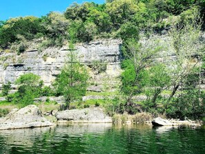 Eine natürliche Landschaft mit einer felsigen Klippe, Bäumen und einem Gewässer.